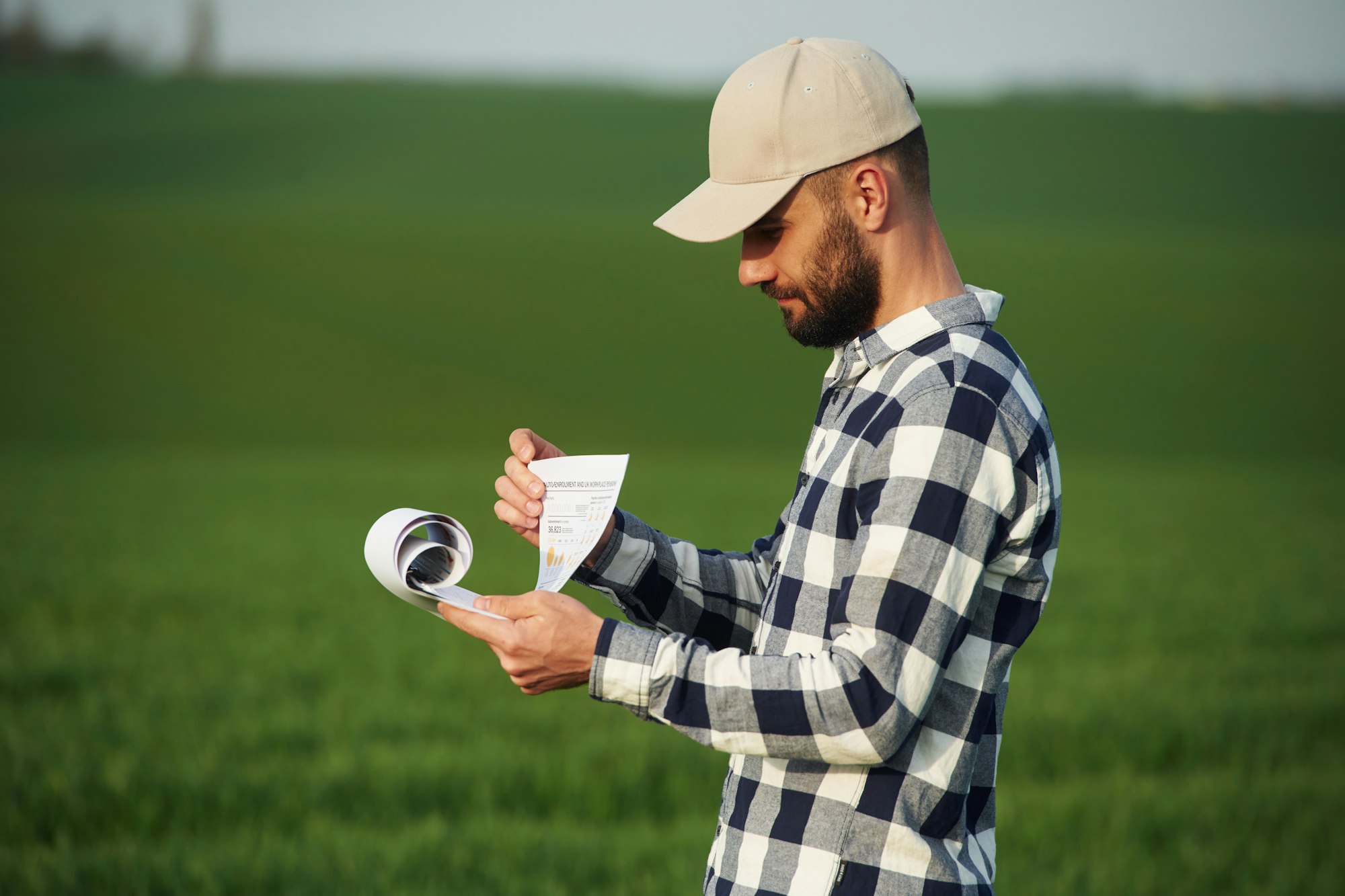 Worker is reading the document. Handsome young man is on agricultural field